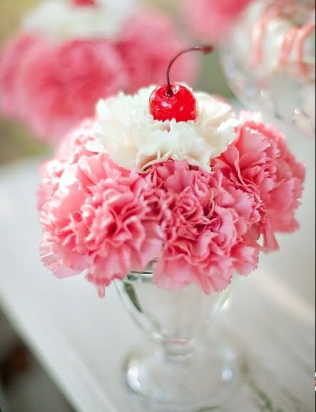 a vase filled with pink carnations and a cherry sitting on top of it