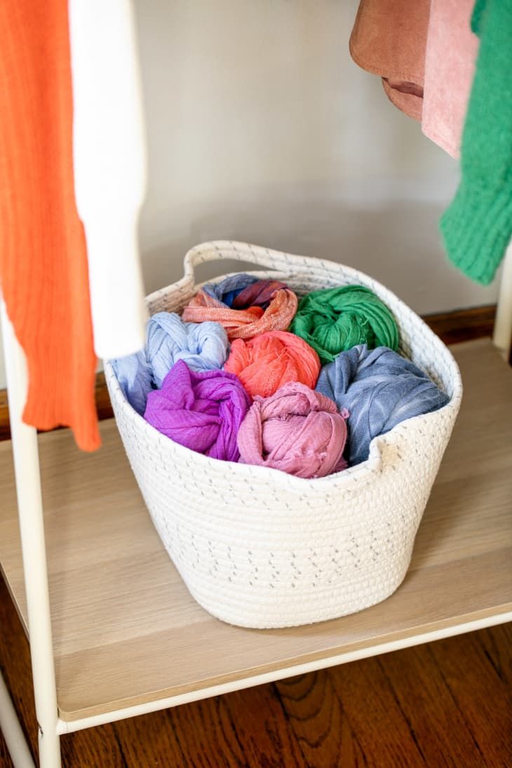 a white basket filled with colorful yarn sitting on top of a wooden shelf next to a coat rack