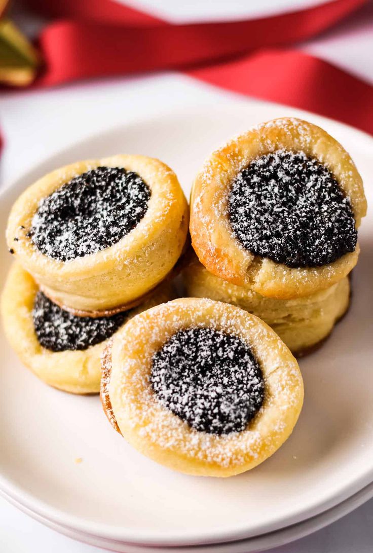 four powdered sugar filled pastries on a white plate next to a red ribbon