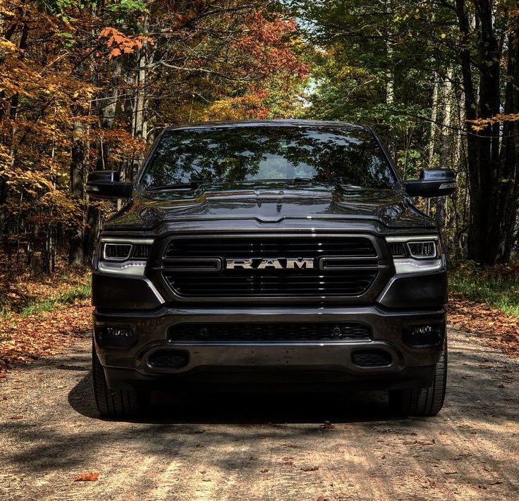 the front end of a black ram truck parked on a dirt road near some trees