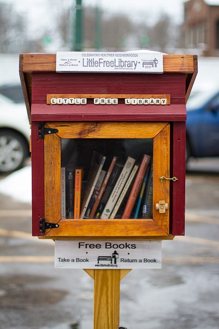 a wooden box with books in it sitting on top of a pole next to a parking lot