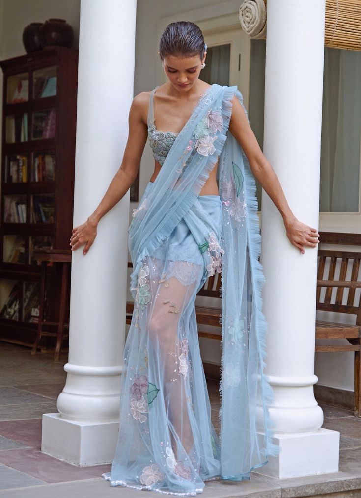 Presenting the stunning Soft Blue Embroidered Net Skirt Saree, a perfect blend of modern elegance and timeless charm. Crafted from soft net and organza fabrics, the sheer tulle blue skirt and pallu are beautifully lined with French lace and silk, creating a delicate yet striking silhouette. Hand-embroidered with intricate organza and 3D beaded flowers, this design exudes a sophisticated floral aesthetic. Paired with a statement corset featuring zardosi-embroidered flowers, organza blooms, and an underlayer of French lace, this ensemble is a true work of art. Playful peek-a-boos of lace and an oversized bow at the back add feminine allure, making it ideal for cocktail parties or evening events. The inner lace detail can be customised as per your style. Composition : Skirt, Pallu and Blouse Fitted Blue Pre-draped Saree With Intricate Embroidery, Blue Organza Pre-draped Saree With Dupatta, Evening Georgette Pre-draped Saree With Floral Embroidery, Evening Pre-draped Georgette Saree With Floral Embroidery, Blue Fitted Tissue Silk Pre-draped Saree, Blue Fitted Pre-draped Tissue Silk Saree, Organza Pre-draped Saree With Floral Embroidery For Reception, Floral Embroidered Organza Pre-draped Saree For Reception, Party Blue Pre-draped Saree With Intricate Embroidery