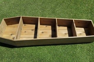 an empty wooden box on the grass with four compartments in each side and one section missing