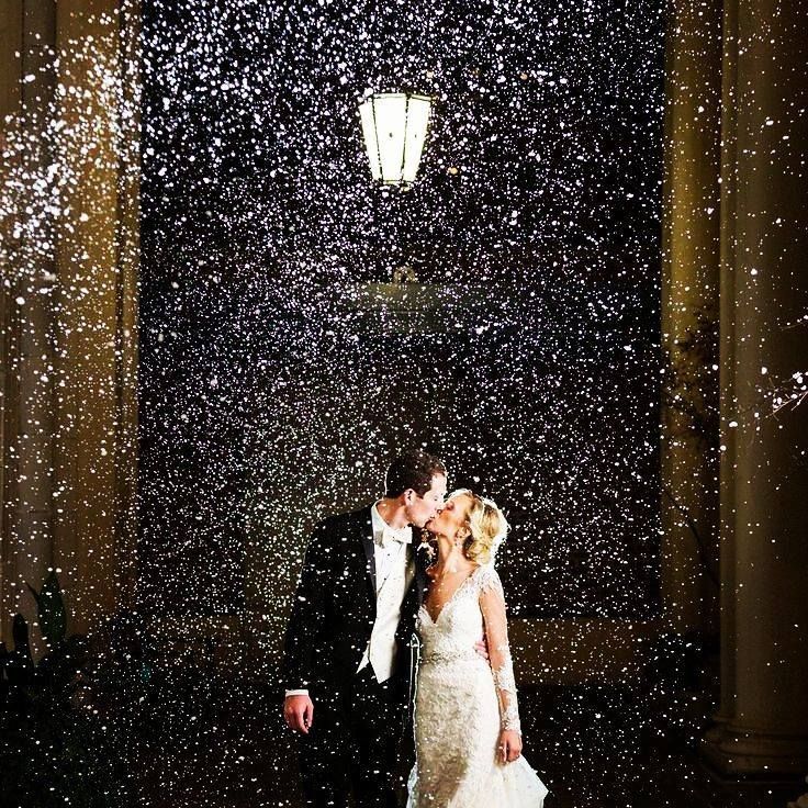 a bride and groom kissing in the rain at their wedding reception with falling snow all around them