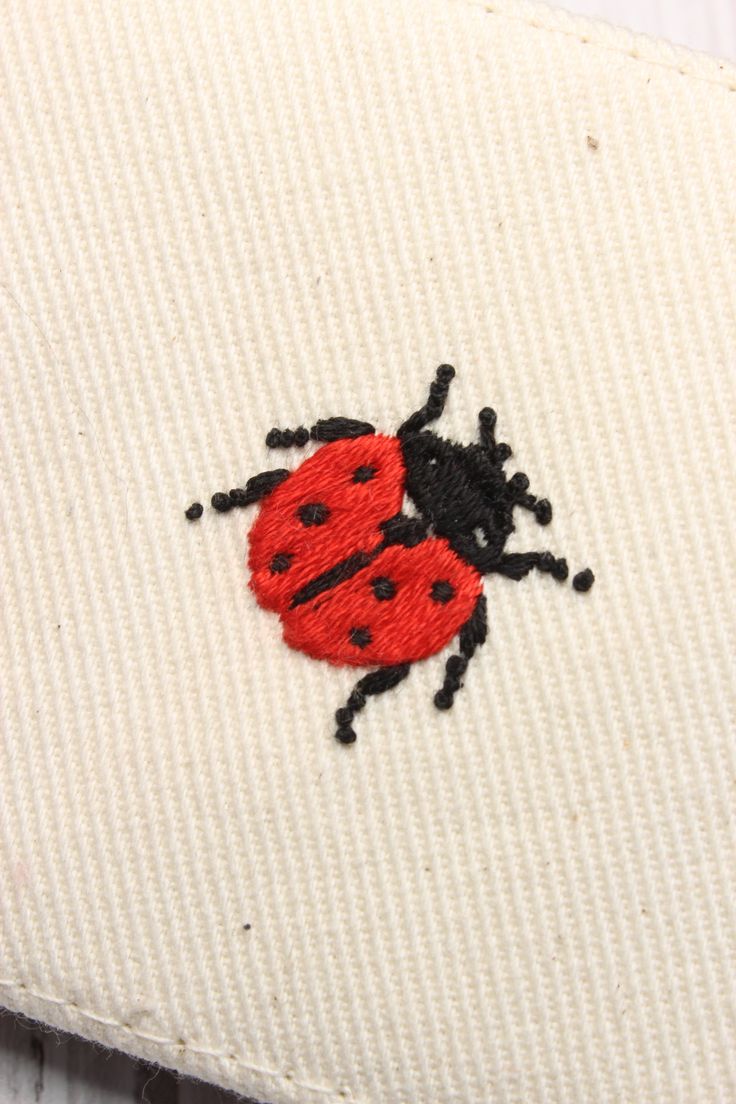 a close up of a red and black ladybug embroidered on a white cloth