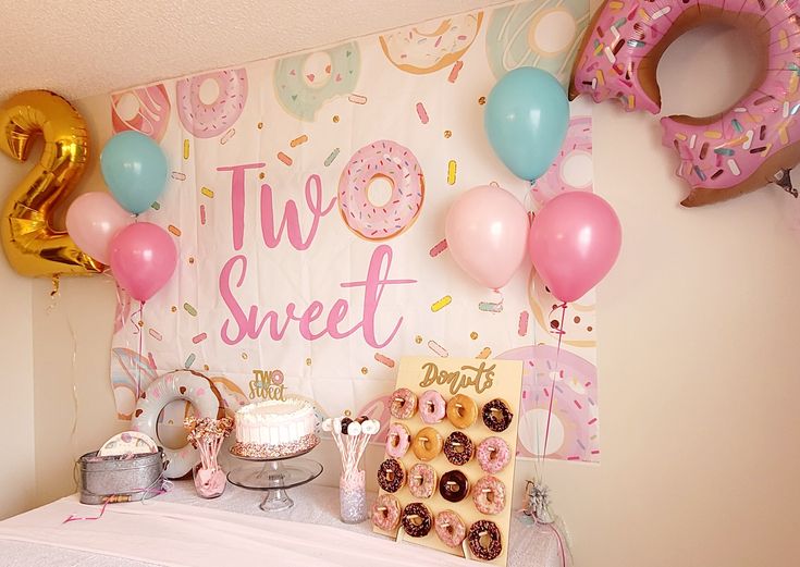 a table topped with donuts and balloons in front of a sign that says two sweet