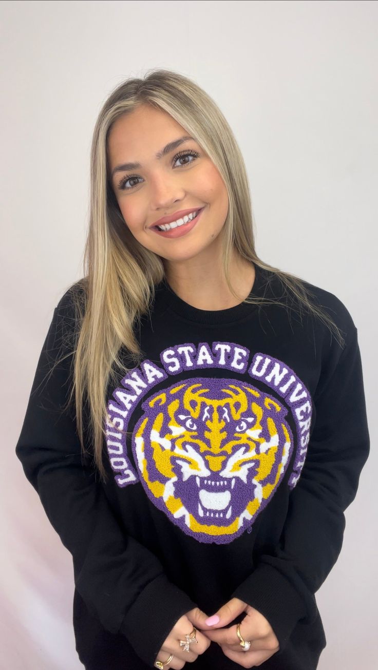 *OFFICIALLY LICENSED BY LSU* The indicia featured on this product are trademarks of Louisiana State University. Louisiana State University (Licensed) | Women's Chenille Embroidery Sweatshirt (Black) Calling all LSU Tigers Fans! Check out this Chenille Embroidery Sweatshirt in stunning purple and gold! *Size Chart available for size reference in the images* Material: French Terry Features: Chenille Embroidery Please Note: We do not re-stock the same design & tee sweatshirt color. Once this item i Black College Sweatshirt With Embroidered Logo, Black Embroidered Logo Sweatshirt For College, Black Varsity Tops With Embroidered Logo, Black College Sweatshirt With Embroidered Graphics, Black Tops With Embroidered Graphics For Fall, Black Embroidered Sweatshirt For College, Black Embroidered Tops For Fall, Black Collegiate Sweatshirt With Embroidered Logo, Black College Sweatshirt With Embroidered Text