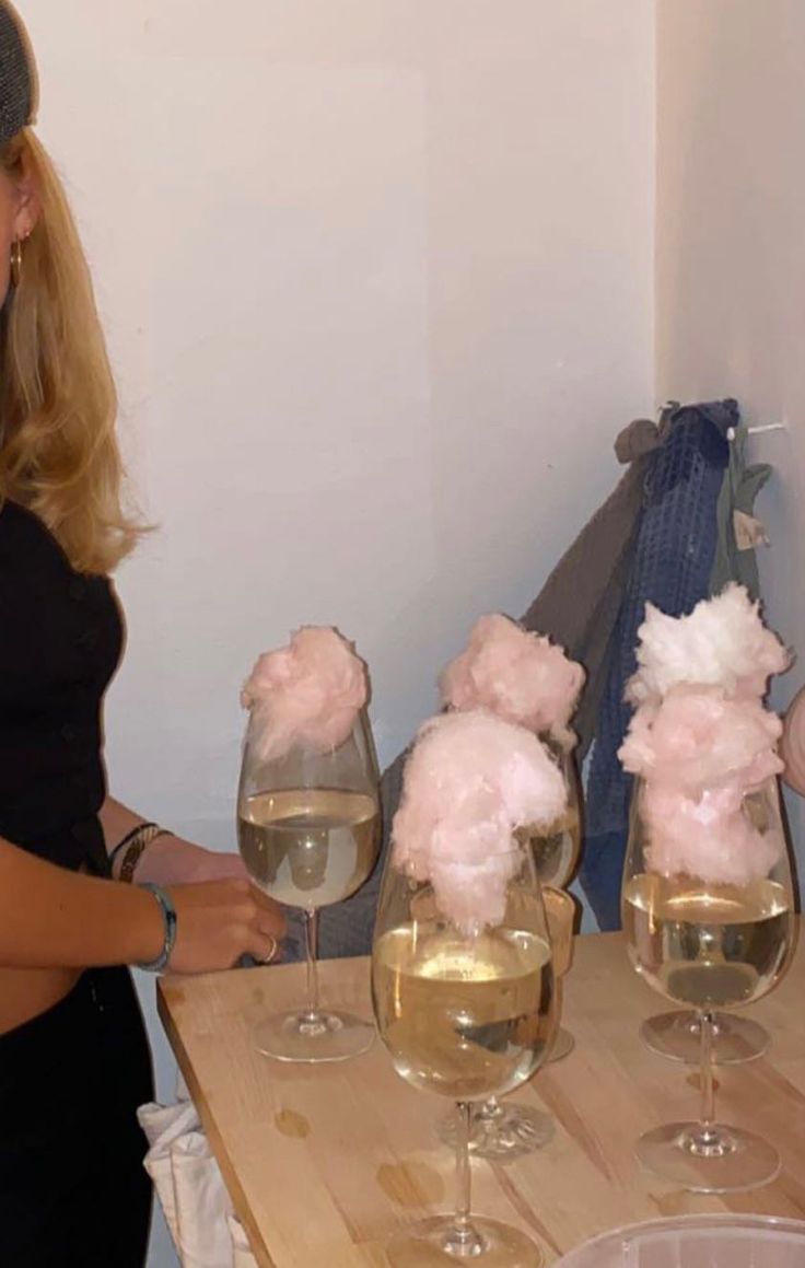 a woman standing in front of three wine glasses filled with water and cotton floss