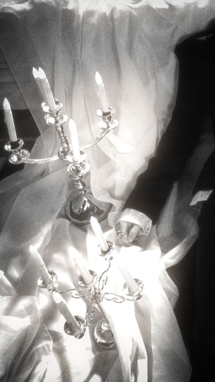 a black and white photo of two candles on a bed with sheer fabric draped over it