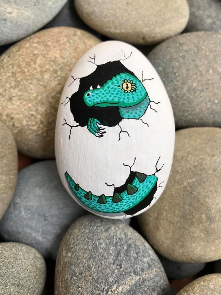 an egg with a lizard painted on it is sitting among some gray and white rocks