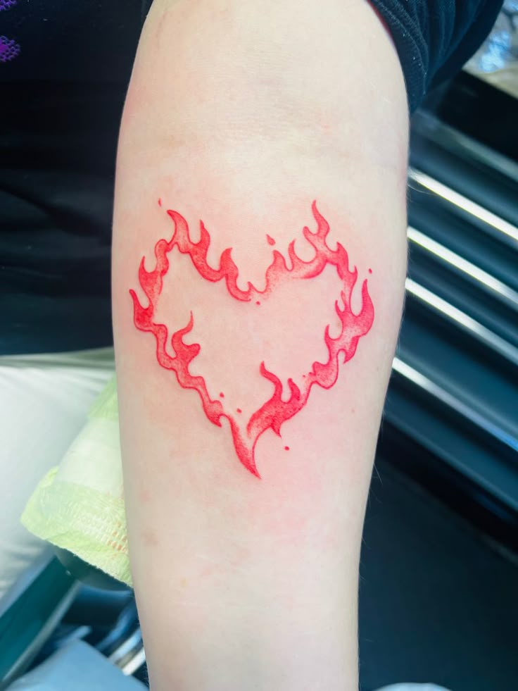 a heart shaped tattoo on the arm with flames coming out of it's center