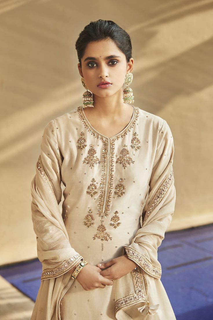 Editor's Note Introducing Sucha Ekru Aurum Sharara Set, an illuminating ensemble with intricate golden embroidery and sequins on Chanderi silk. The kurta features quarter sleeves and bootie detailing on the neckline, paired with airy sharara pants with Dori work at the hem. Complete with a flamboyant monotone organza dupatta adorned with heavy tassels and bootie patchwork. Fabric: Chanderi silk Color: Ivory Components: Sharara, kurta and dupatta Disclaimer: Product colour may slightly vary due t Minimal Embroidery Design, Minimal Embroidery, Designer Suits For Wedding, Silk Sharara, Design Kurta, Sharara Pants, Trendy Suits, Ivory Colour, Sharara Set