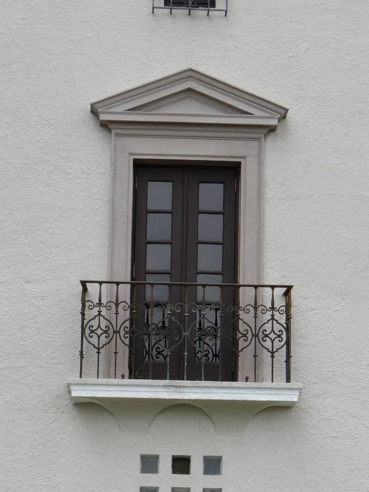 an open window on the side of a white building with wrought iron balcony railings