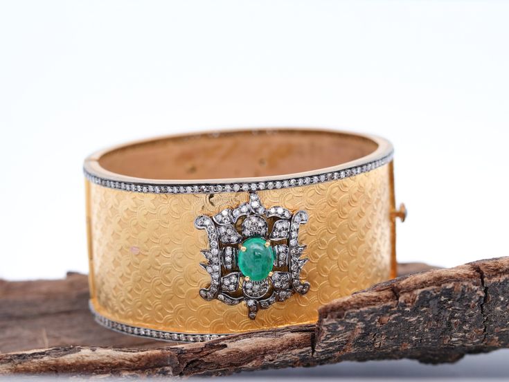 Discover Uniqueness in Every Detail with our Two-Tone Diamond and Emerald Bangle One of a Kind Design: This exquisite bangle is a true work of art, featuring a stunning textured design. It's expertly set in a combination of 14kt Yellow Gold and Sterling Silver, adorned with Pave Diamonds and lustrous Emeralds. The intricate scallop texturing and the motif design housing Diamonds and Emeralds make this bangle a truly unique piece of jewelry. The cuff opens from the side, and the closure is adorned with Diamond Polki, adding to its allure. The two-tone effect of the metals ensures this bangle stands out in any crowd. Details: - Gross Weight: 57.72 gms - 14k Gold Weight: 48.00 gms - Silver Weight: 7.23 gms - Diamond Weight: 4.10 cts - Emerald Weight: 8.60 cts - Dimensions:   - Inner Diameter: Luxury Jeweled Bangle, Luxury Jeweled Bangle Cuff Bracelet, Luxury Jeweled Bangle For Formal Occasions, Elegant Cuff Jewelry With Intricate Design, Wedding Cuff Bracelet With Diamond Accents, Formal Hand Set Cuff Bracelet, Elegant Ceremonial Cuff Bracelet, Fine Jewelry Diamond Accents Bangle For Wedding, Formal Gemstone Cuff Bracelet In Bangle Shape