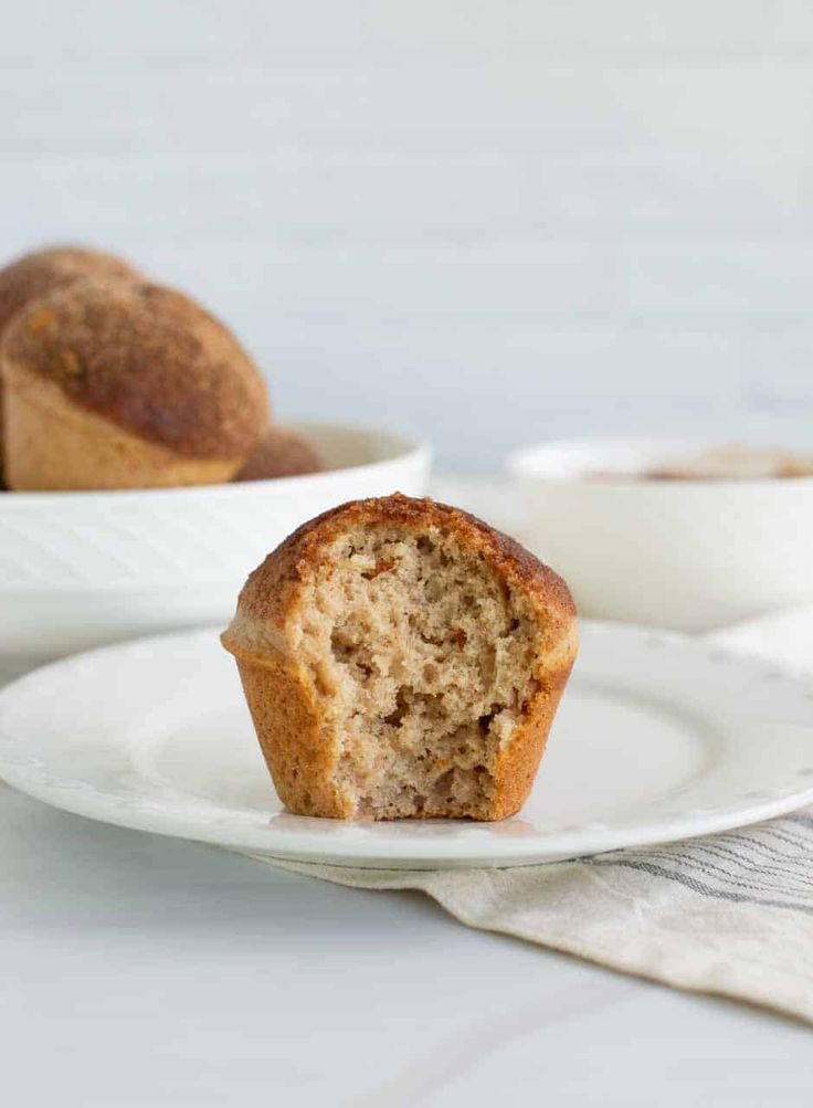 a muffin on a white plate with another muffin in the background