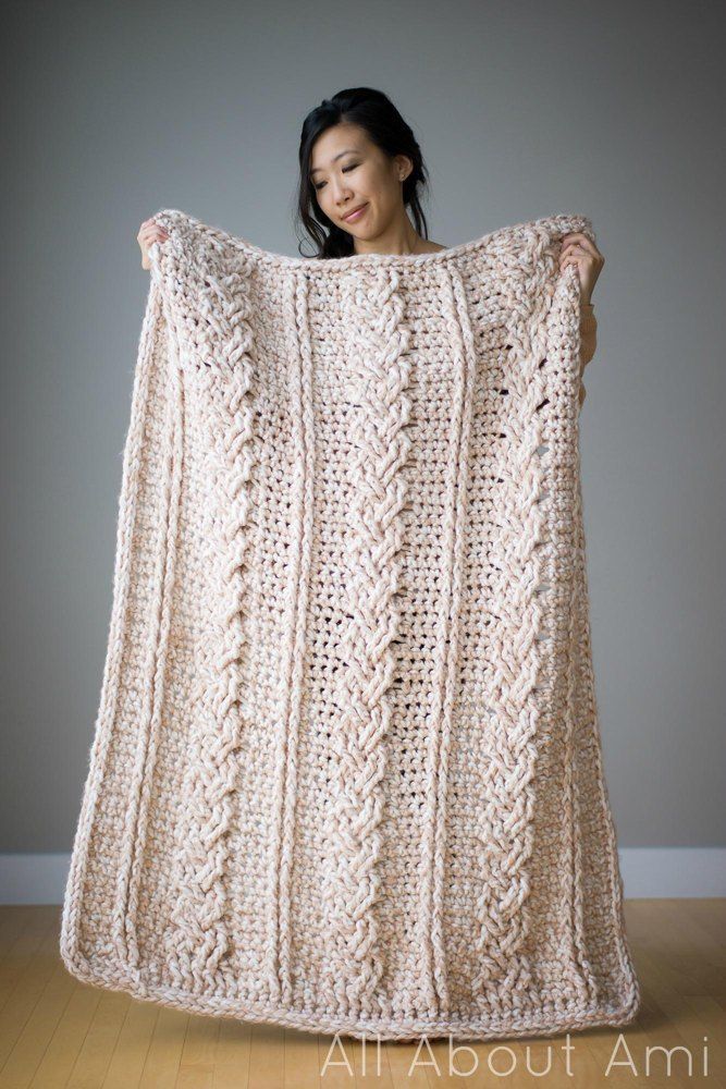 a woman is holding up a crocheted blanket