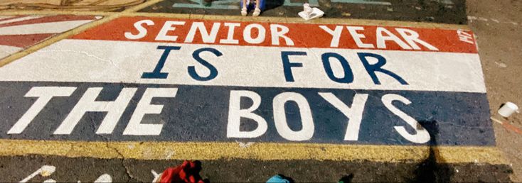 a sign painted on the ground that says senior year is for the boys and two children are standing in front of it