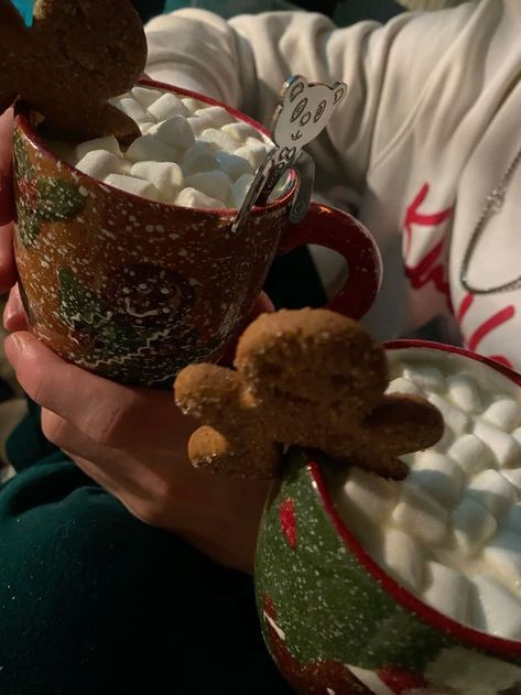 two people holding mugs filled with marshmallows and cookies