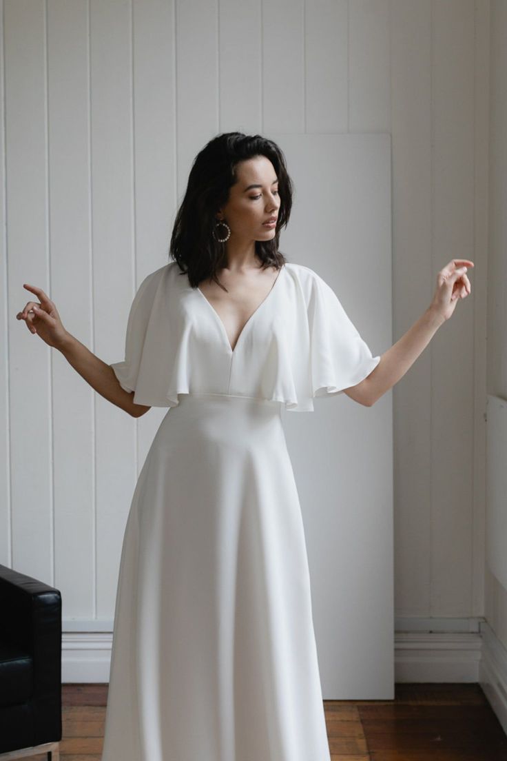 a woman in a white dress standing on a hard wood floor with her arms outstretched