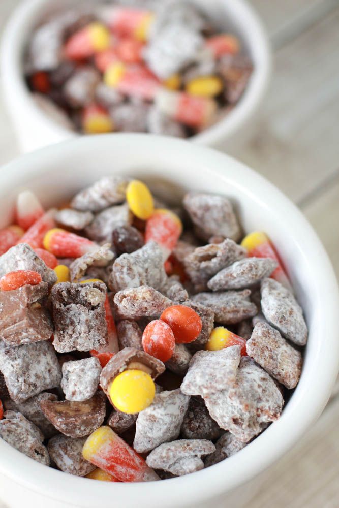 two white bowls filled with candy corn and chocolate puppy chow treats on top of a wooden table