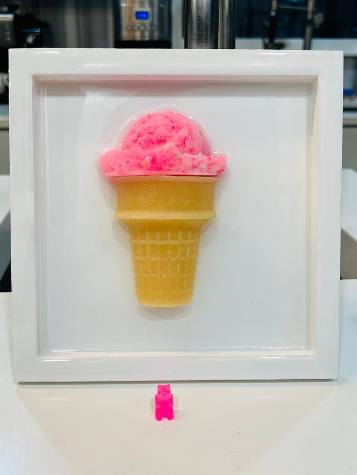 an ice cream cone with pink sprinkles in a white frame on a counter