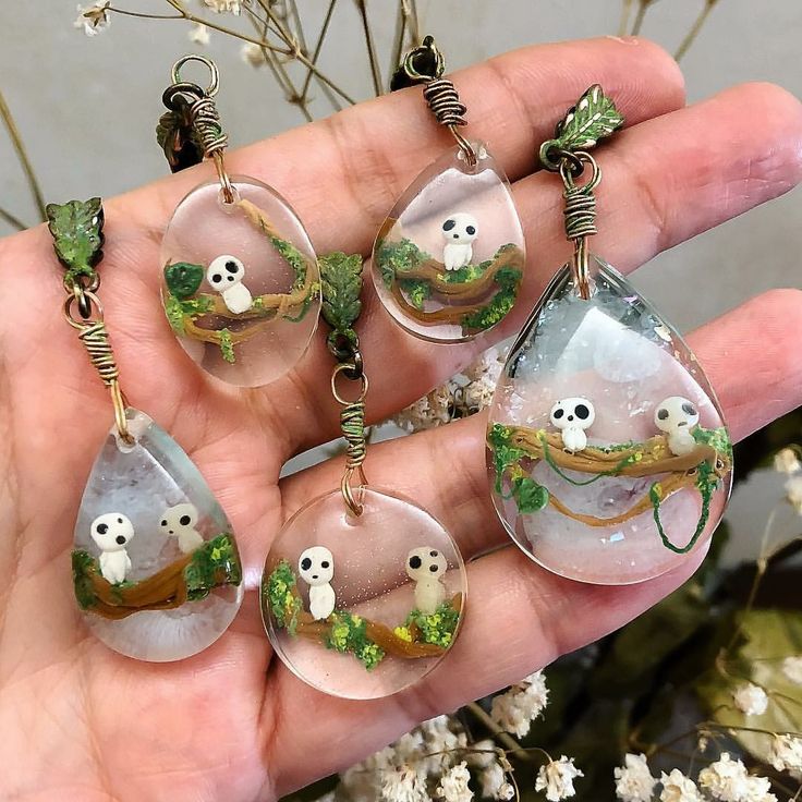 a hand holding six glass pendants with animals inside them and trees in the background