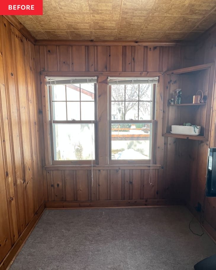 an empty room with wood paneling and two windows