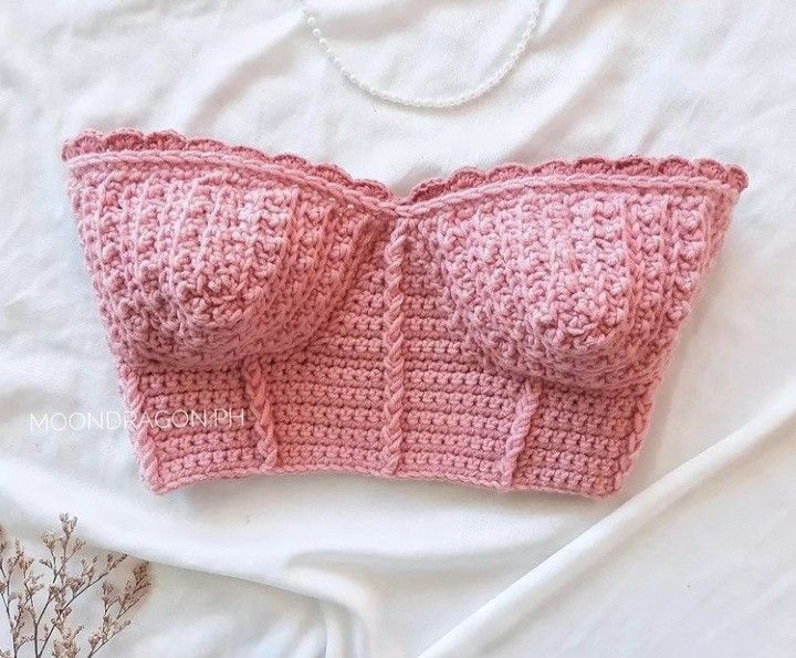 a pink crocheted bra laying on top of a bed