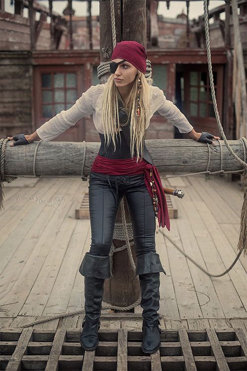 a woman with long blonde hair standing on a wooden deck wearing pirate garb and boots