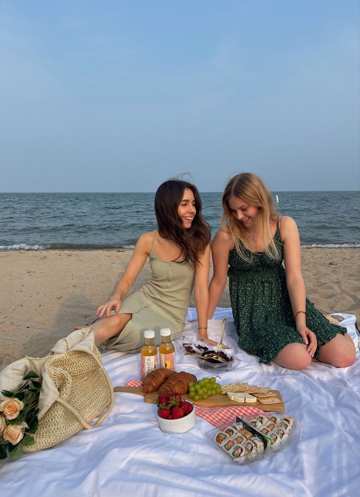 two women sitting on the beach with food