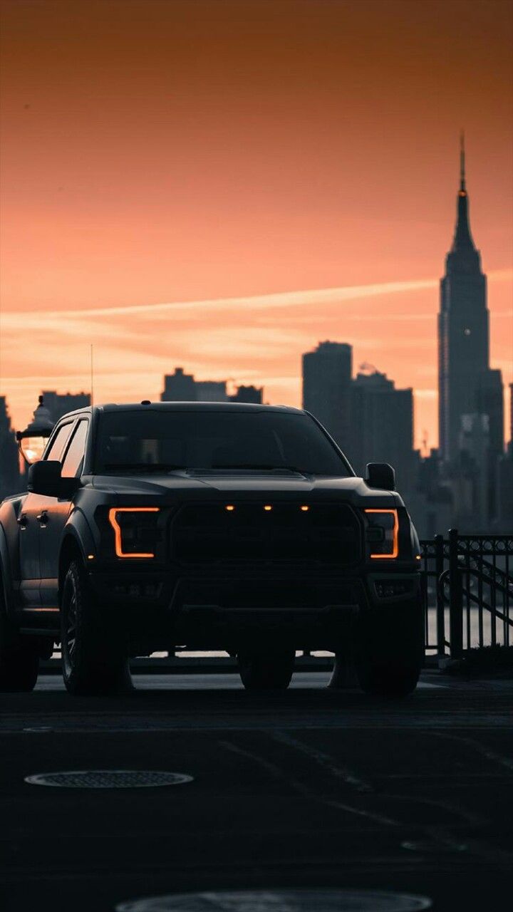 the truck is driving down the road in front of the cityscape at sunset