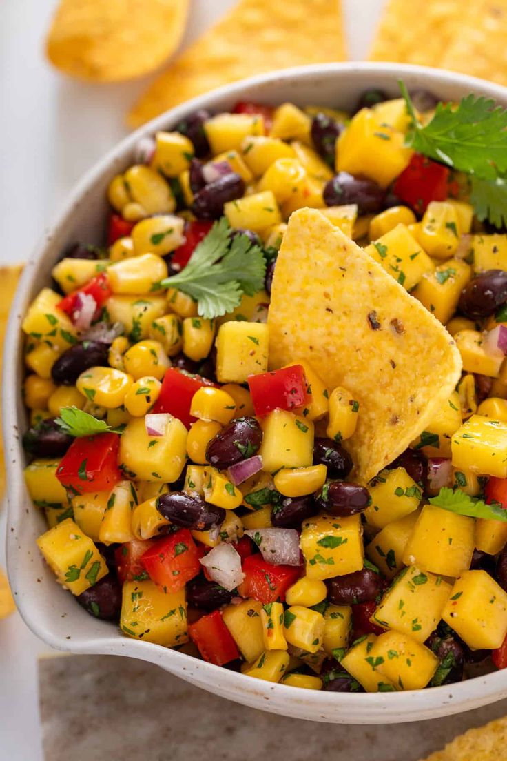 a white bowl filled with black beans, corn and mango salsa surrounded by tortilla chips