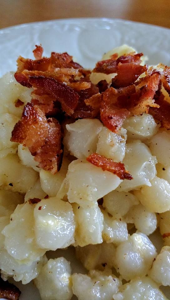 a white plate topped with macaroni and cheese covered in bacon on top of a wooden table