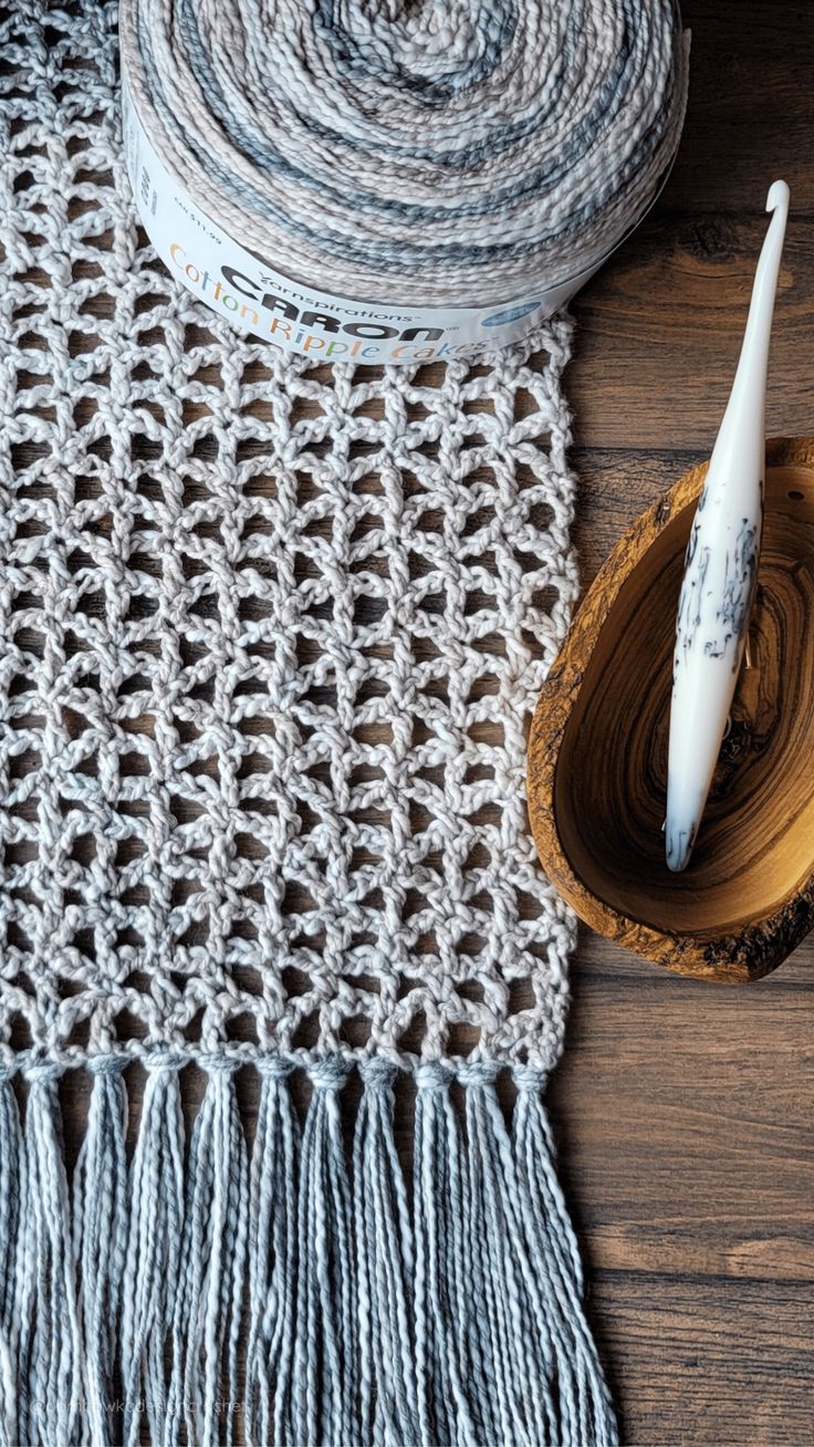 a knitted table runner next to a wooden bowl with yarn in it and a white crochet brush