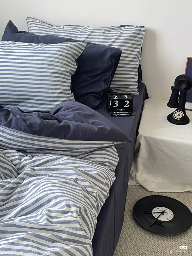 there is a bed with blue and white striped sheets on it, next to an alarm clock