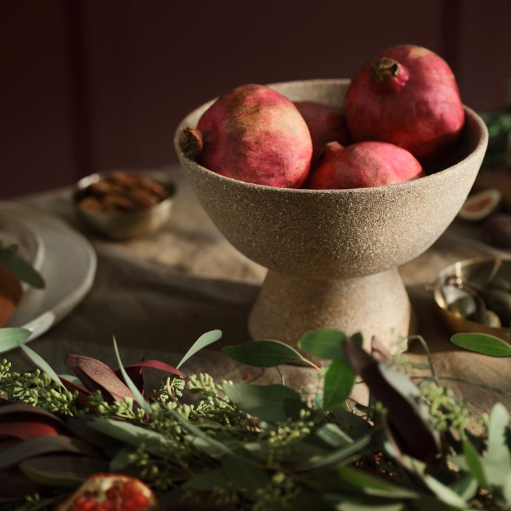 a bowl filled with red fruit sitting on top of a table covered in greenery