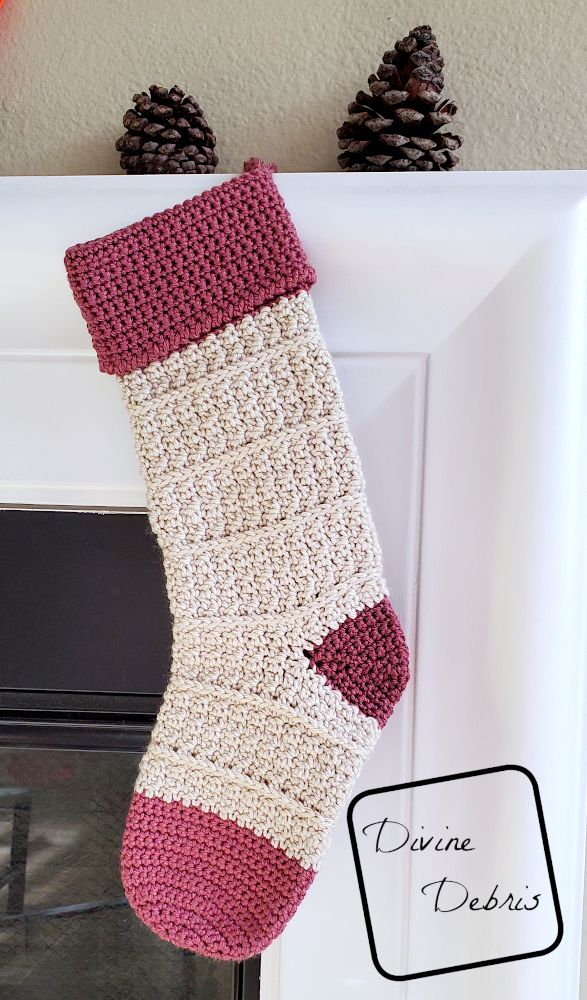 a crocheted stocking hanging from a fireplace with pine cones in the background