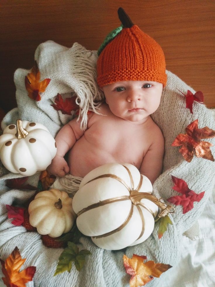 a baby wearing a knitted hat and sitting in a basket with pumpkins on it