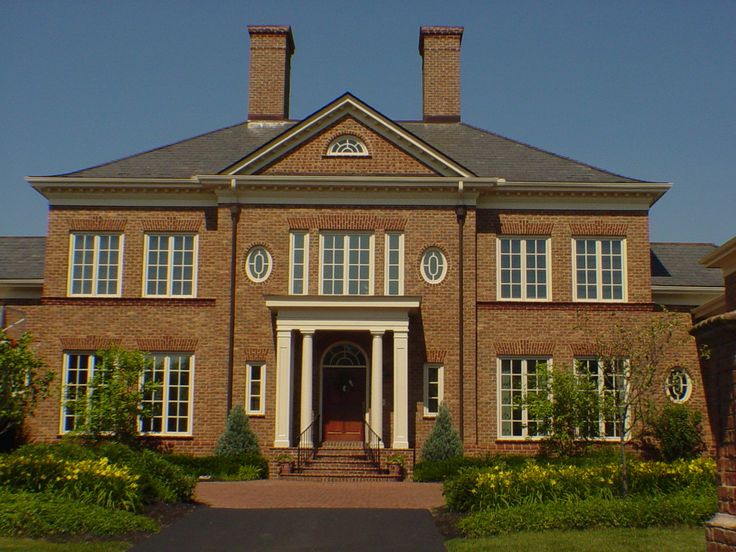 a large brick house with white trim and arched windows on the front door, surrounded by greenery