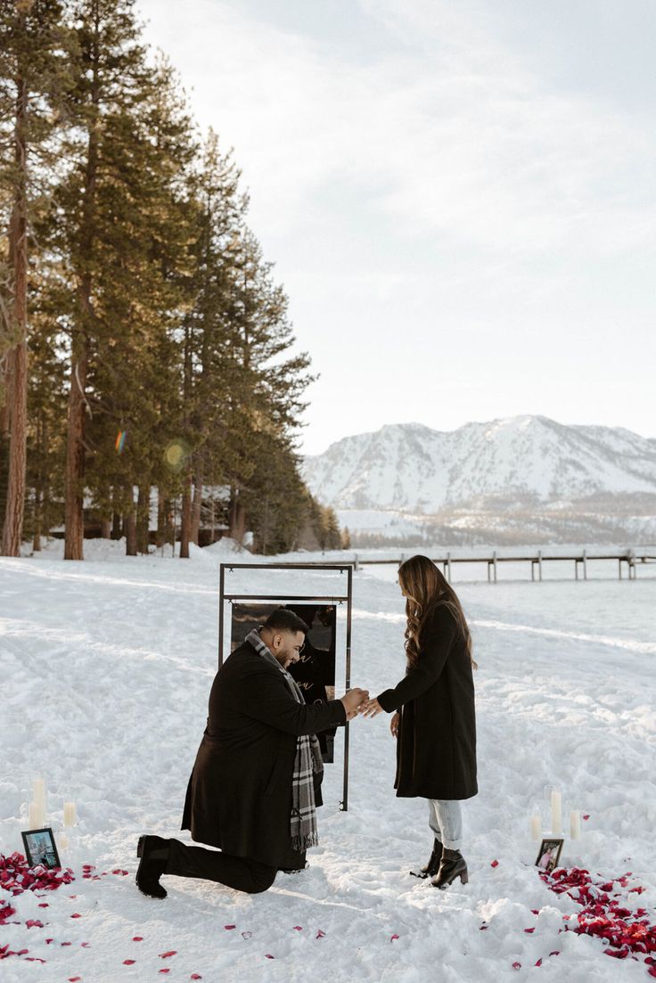 a man kneeling down in the snow next to a woman who is touching her hand