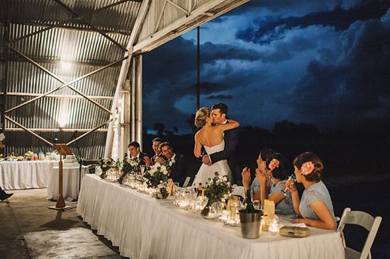 a bride and groom kissing in front of their guests at a dinner table with candles on it