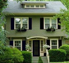 a green house with black shutters and white trim on the front door is surrounded by greenery