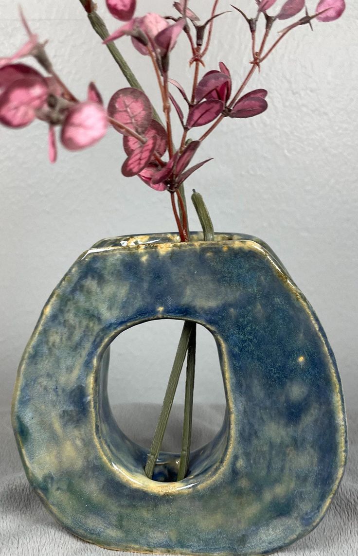 a blue vase with pink flowers in it on a white tableclothed surface next to a wall