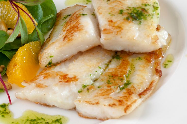 some fish is on a white plate with green garnish and oranges next to it