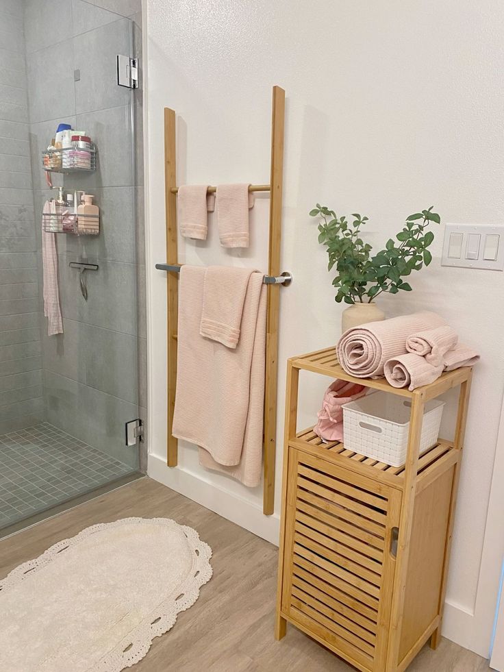 a bathroom with a stand up shower next to a white rug and towel rack on the floor