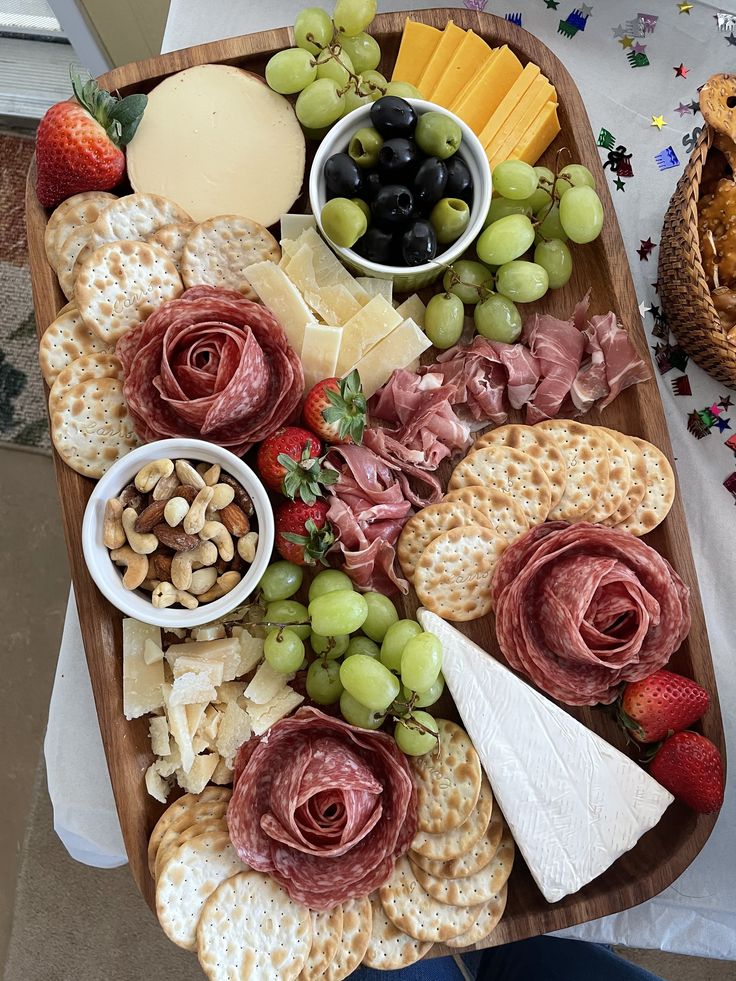 a wooden platter filled with cheese, crackers, grapes and other food items