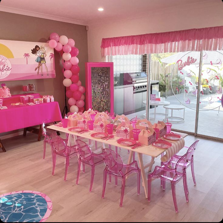 a table set up for a birthday party with pink decorations and balloons on the wall