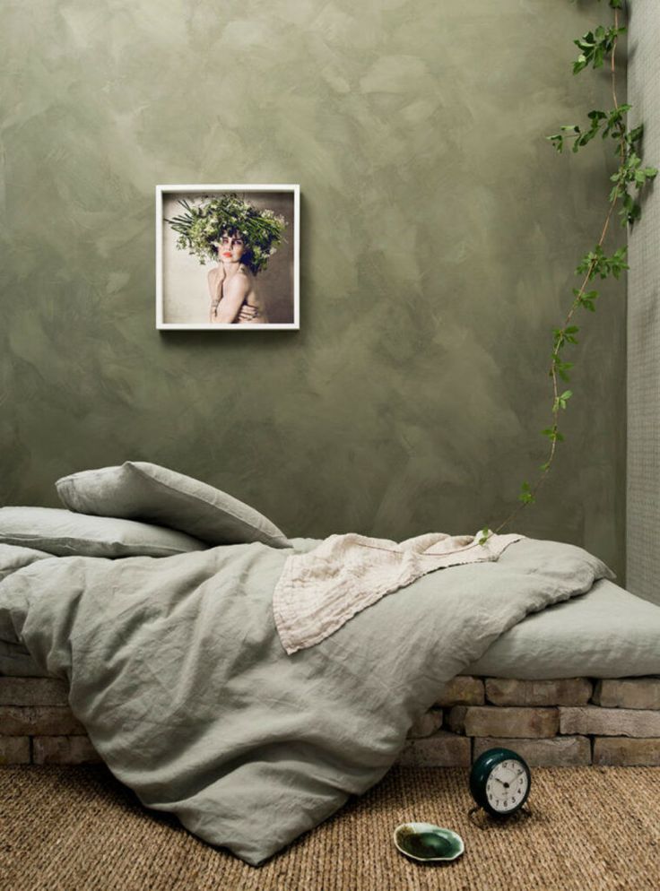 an unmade bed sitting on top of a floor next to a clock and plant