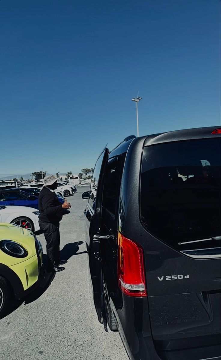 a man standing next to a yellow and black car in a parking lot with other cars