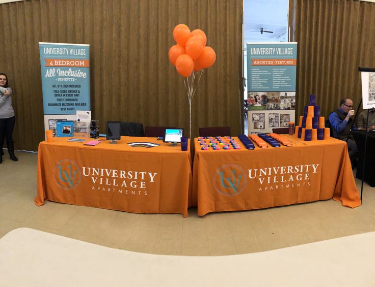 an orange table topped with lots of balloons next to a sign that says university village